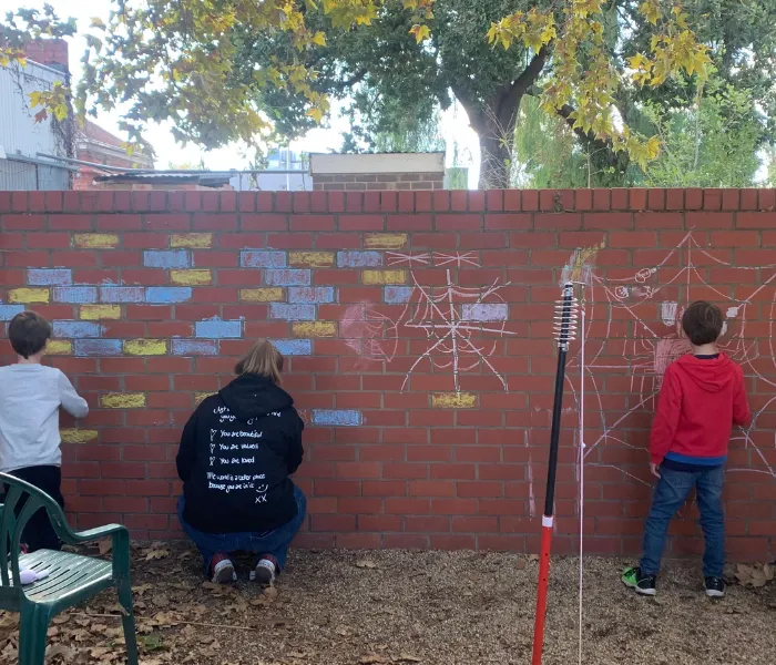 Support worker with two young children drawing on brick wall with chalk