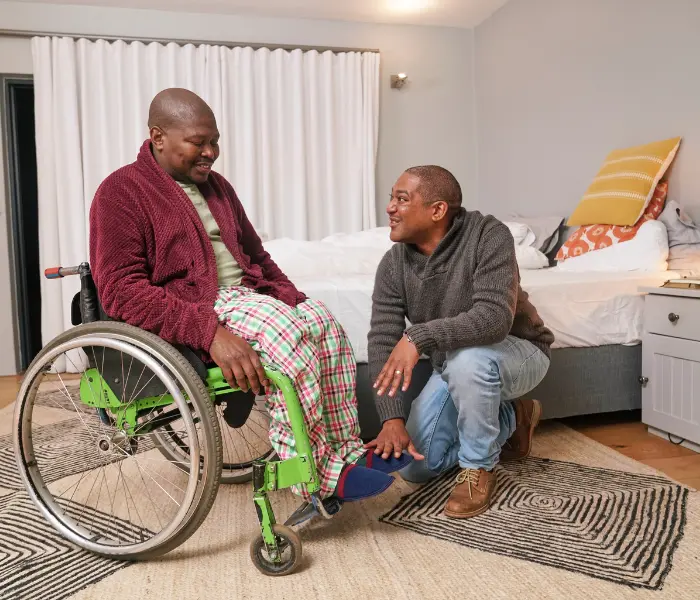 Disabled man in wheelchair in bedroom with support worker helping put slippers on