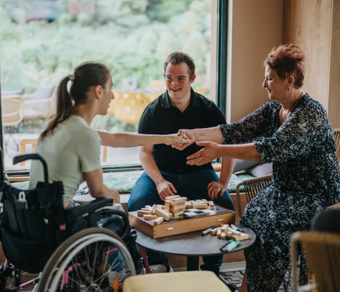 Support worker sitting with two disabled individuals, one in wheelchair, all playing a game