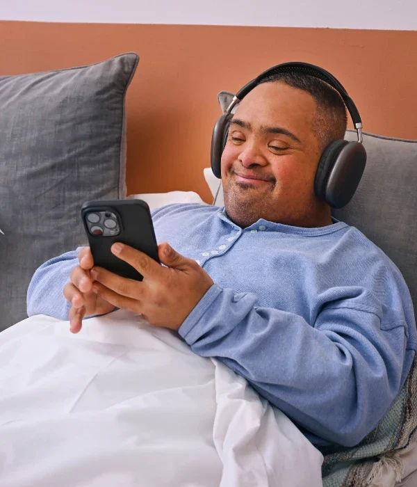 Disabled man in bed using mobile phone with headphones and smiling