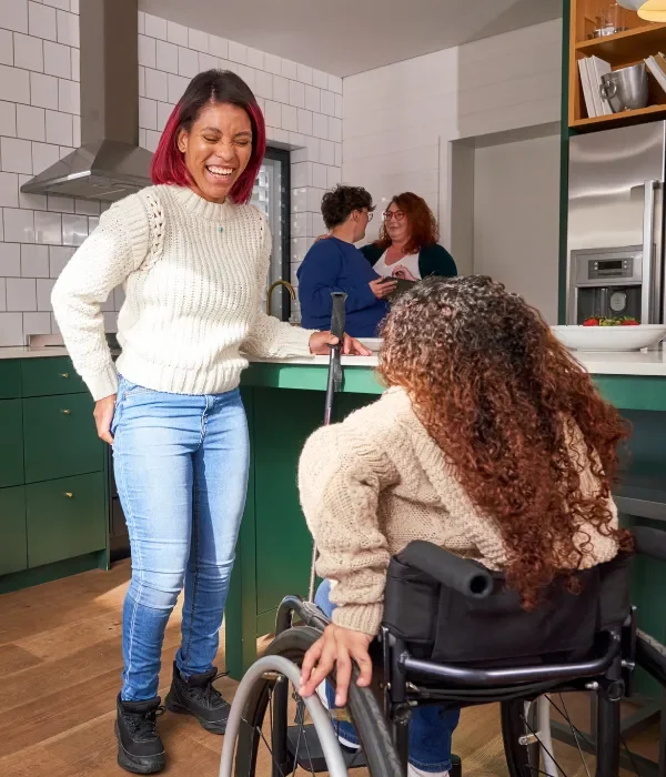 Disabled woman in wheelchair laughing with friend in kitchen
